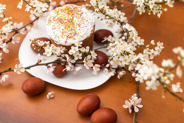 Easter composition. A blooming apricot branch, painted eggs and a glazed Easter cake decorated with sugar sprinkles