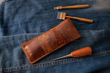Vintage Handmade Leather pencil case. Leathercraft tools with a denim background.	