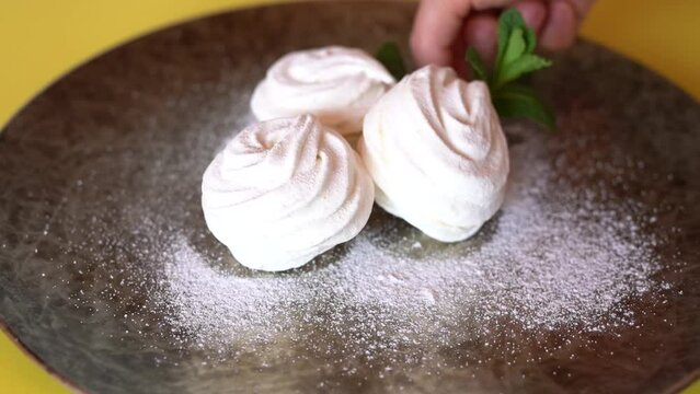 Delicious white marshmallow on a plate with powdered sugar is decorated with flowers.