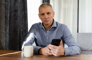 Portrait of a male businessman who sits at a table, holds a phone in his hands, looks into the camera