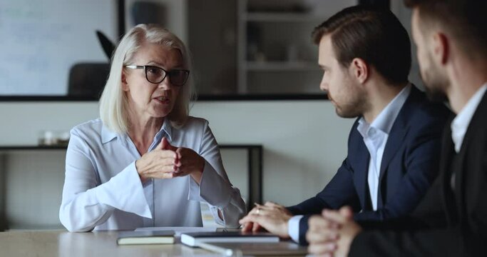 Elderly and millennial colleagues, business partners engaged in formal negotiation, planning joint business and future cooperation seated at desk in company office. Meeting of client and sales manager