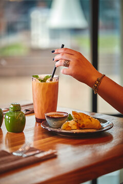 Woman's hand holds glass with milkshake or smoothie on wooden table in cafe against the background of window