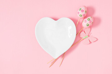 Easter holiday composition. Easter decorations, heart shaped plate on pastel pink background. Easter concept. Flat lay, top view, copy space
