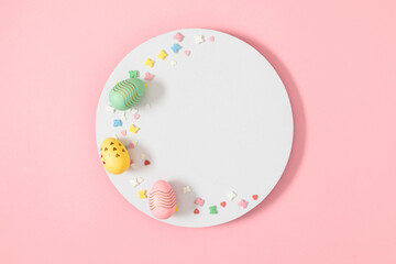 Easter celebration composition. Top view of blank white circle, easter eggs and colorful sugar candy sprinkles isolated on pastel pink background. Easter concept. Flat lay, top view, copy space 