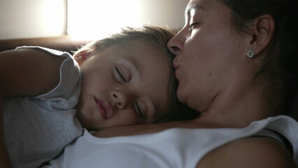 Obraz na płótnie Canvas Mother kissing sleeping child in forehead while napping. Parent and little boy son asleep together