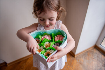 Top view close up portrait Little curly girl holds heart shaped box with homemade