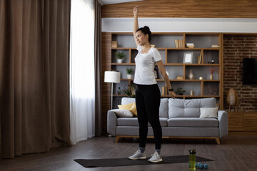 Beautiful young woman in sport outfit spending free time at home for active fitness exercises. African dark haired female training muscles on back and hands.