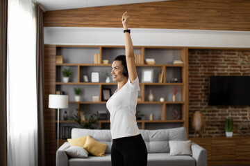 Attractive interracial woman in activewear listening music in wireless headphone during morning exercises at apartment. Happy young lady enjoying active and healthy time spending alone at home.