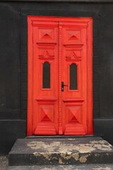 Antique wooden door, bright red color with carved patterns on a black wall