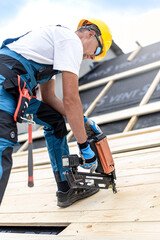 The carpenter nails a timber board using an electric nailer while working on a roof.