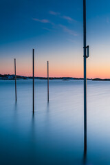 Poles standing in sea at sunset