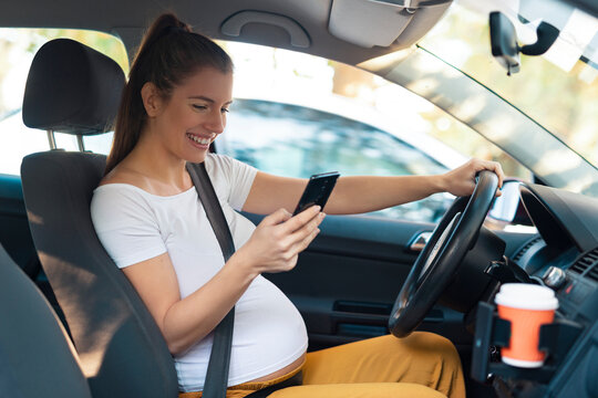 Pregnant woman is using mobile phone while driving the car