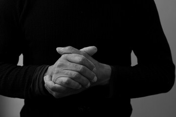 man praying to God with hands together on grey black background with people stock photo