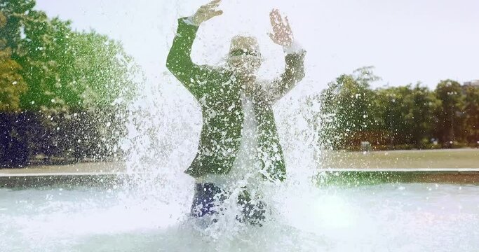 Carefree Young Man Standing in water fountain chilling in summer time