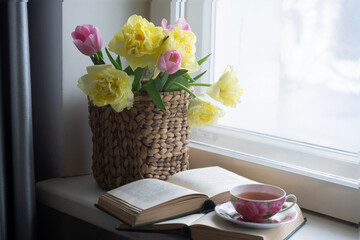 Tulips, a cup of hot tea and a book on the table.