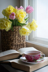 Tulips, a cup of hot tea and a book on the table.