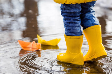 It's springtime. A small child in yellow rubber boots jumps through puddles, plays and launches...