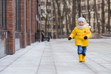 Portrait of a small child 4 years old in yellow rubber boots and a jacket. The kid walks in the park in the spring. Photo of spring and autumn holidays.