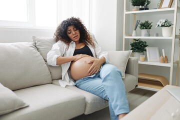 Obraz premium Pregnant woman headache lies at home in a shirt and jeans on the couch fatigue and heaviness in the last month of pregnancy before childbirth, motherhood difficulties, nausea