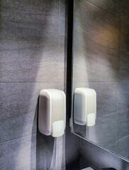 Wall dispenser liquid soap dish in modern bathroom in front of mirror on granite wall. Modern...