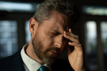 Tired man having a terrible headache. Exhausted man feeling unhealthy, upset about headache illness. Stressed middle-aged man having headache. Migraine and headache concept.