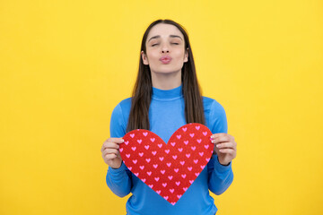 Portrait of attractive lovely cheerful girl holding in hands paper heart, isolated over yellow background. Love valentine concept.