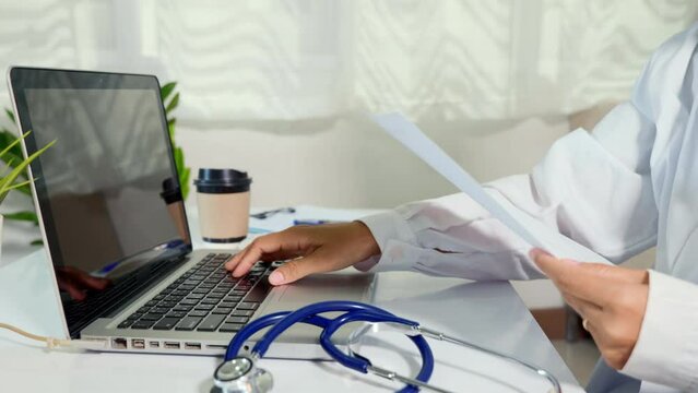 Doctor or nurse woman in uniform with stethoscope working she typing information of patient prescription from paperwork medical history form into laptop computer for record document data report