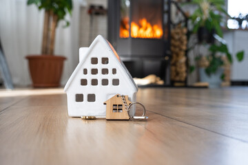 Key to house with keychain against background of fireplace stove with fire and firewood. Cozy home hearth. Building, design, project, moving to new house, mortgage, rent and purchase real estate