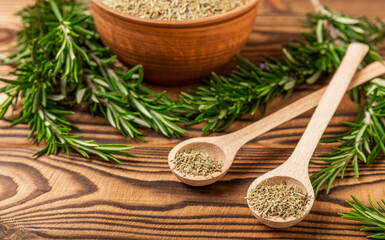 Dried rosemary in wooden spoons and bowl, branches of fresh rosemary on a brown wooden...