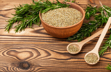 Dried rosemary in wooden spoons and bowl, branches of fresh rosemary on a brown wooden background.Spices and herbs for meat and fish.Recipe.Culinary concept.Organic herbs. Place for text.
