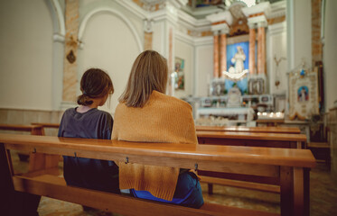 Two women are sitting on a bench in a church.