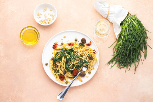 Spaghetti  with Italian Agretti, Barba di frate or Saltwort or  Salsola Soda, olives, anchovy, tomatoes, capers,&nbsp;&nbsp;pine nuts and olive oil, spring Italian recipes. Pink soft spring background