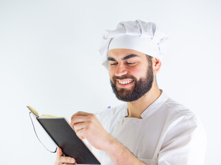 Young male chef using a notebook, writing a recipe. Isolated on a white background