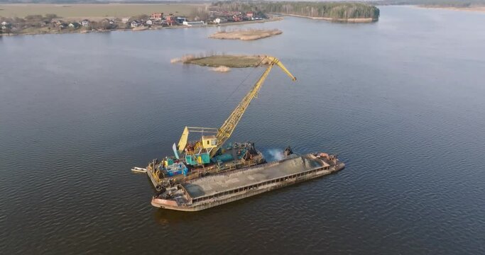 circular flight and aerial view on crane extracts minerals from bottom onto huge barge in middle of lake or sea