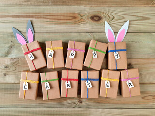 Composition of Easter gifts. Flat lay. Preparing for holiday with children. Craft packaging. Gift boxes with easter decor with bunny ears and tags with the inscription Happy Easter on wooden table