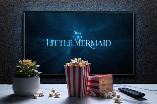TV screen playing The Little Mermaid trailer or movie. TV with remote control, popcorn boxes and home plant. Moscow, Russia - March 20, 2023.