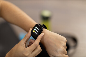 Fototapeta premium Close-up of young african american woman setting her modern smartwatch while sitting with bottle and headphones on floor. Active lady analysing valuable health and fitness data on activity tracker.