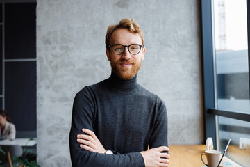 A young red-haired guy, a programmer or an entrepreneur in glasses, in a stylish cafe Looks at the...