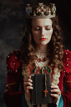 medieval queen in red dress with book, rosary and crown