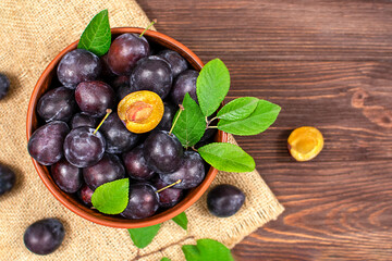 Blue plum in a bowl on a wooden table. Plums in the cut. Top view, place for text. Fruit background with copy space.
