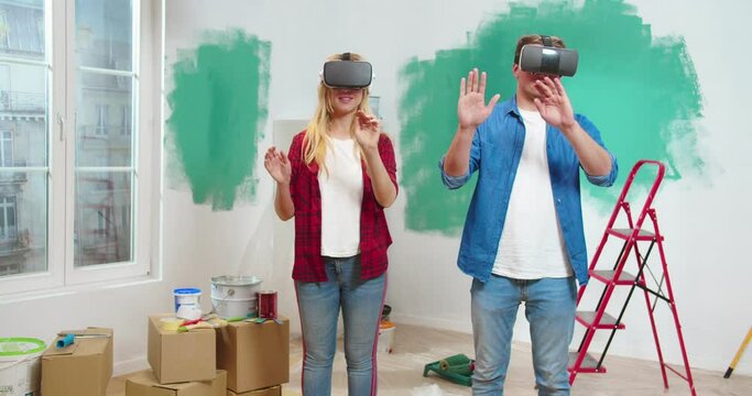 Portrait of beautiful modern caucasian lovely family of man and woman wearing VR helmets and using augmented reality technologies to design future renovation of flat. Virtual reality concept.