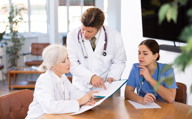 Adult man, elderly woman and young woman doctors having discussion at table