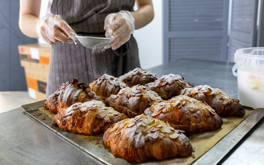 Decoration of almond-flavored croissants with powdered sugar in a bakery