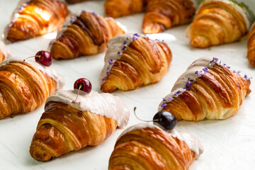 The row of cherry-flavored and violet-flavored croissants half covered with white chocolate in a row in a bakery