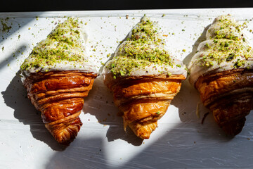 Pistachio-flavored croissants half covered in white chocolate. Beautifully decorated croissants in a bakery