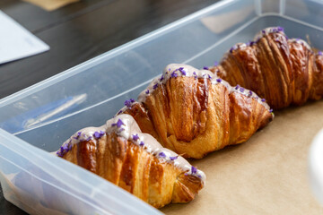 Violet-flavored croissants half covered in white chocolate packed in a box for delivery from the bakery
