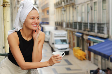 Young beautiful woman in a towel on head is drinking coffee or tea and smiling cute standing on...