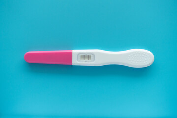 White Plastic Pregnancy test positive with two stripes results isolated on Pastel light blue background. Closeup. Top down view.