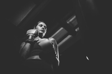 Fototapeta na wymiar Dark Haired Girl Boxing a Punching Bag in a Moody Setting