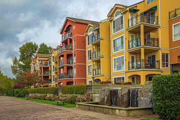 Residential complex in Downtown of New Westminster City with pond in the yard , orange and yellow buildings with flowerbed and green bushes at the front